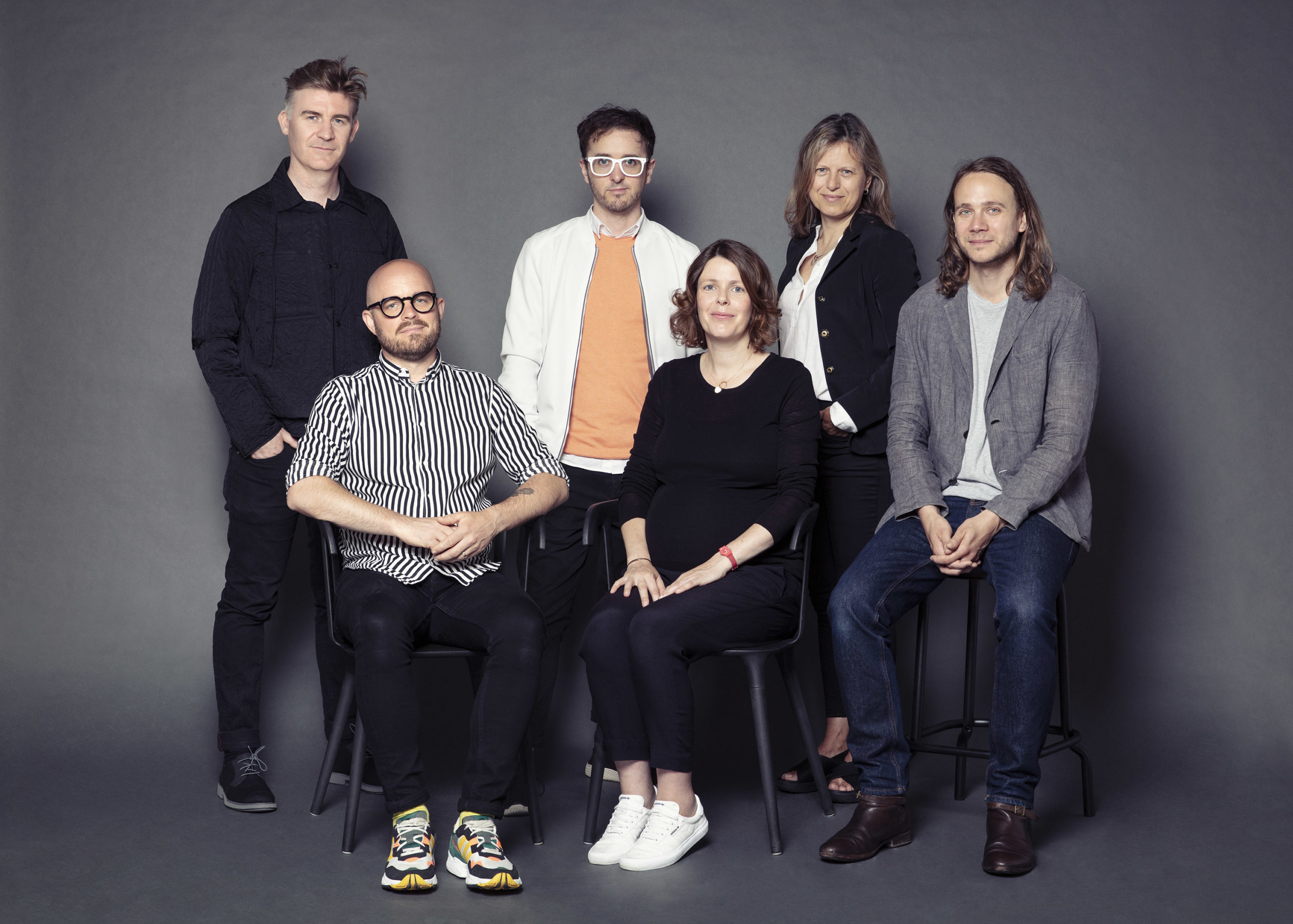 A photo of the Annex team, taken against a grey background. There are four men and two women. Four figures are standing, while two remain seated.